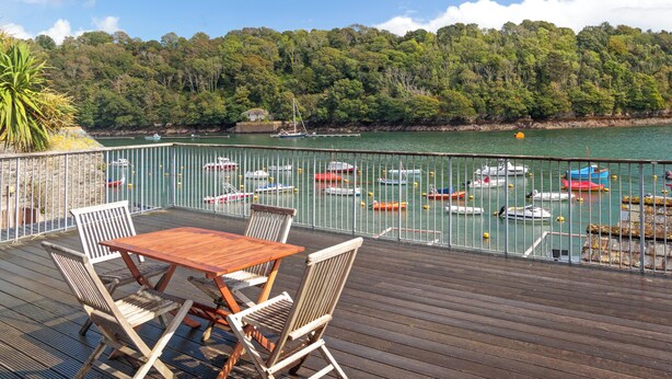 Una terraza de madera con mesa y sillas que da a un puerto deportivo con varias embarcaciones.
