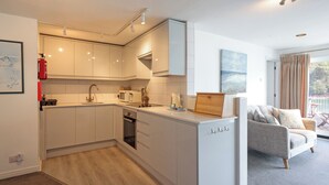 Una cocina moderna con armarios blancos, horno integrado y comedor con sofá gris y aparador de madera.