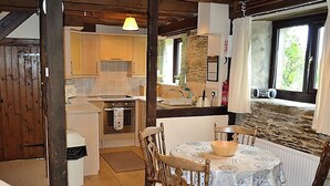 A rustic kitchen with wooden beams, a stone wall, and a dining area with a round table and chairs. - 2 bedroom accommodation in Fowey (Fowey)