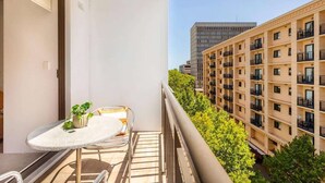 Un balcon avec une table et des chaises, un pot de fleurs et une vue sur les bâtiments voisins.