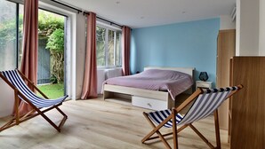 Une chambre à coucher avec un lit, deux chaises à rayures, une fenêtre avec des rideaux et une vue sur la verdure à l’extérieur.