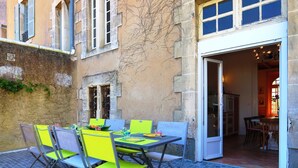 Un espace extérieur aménagé pour les repas, avec une table et des chaises, un mur en pierre et une porte-fenêtre donnant sur un espace intérieur.