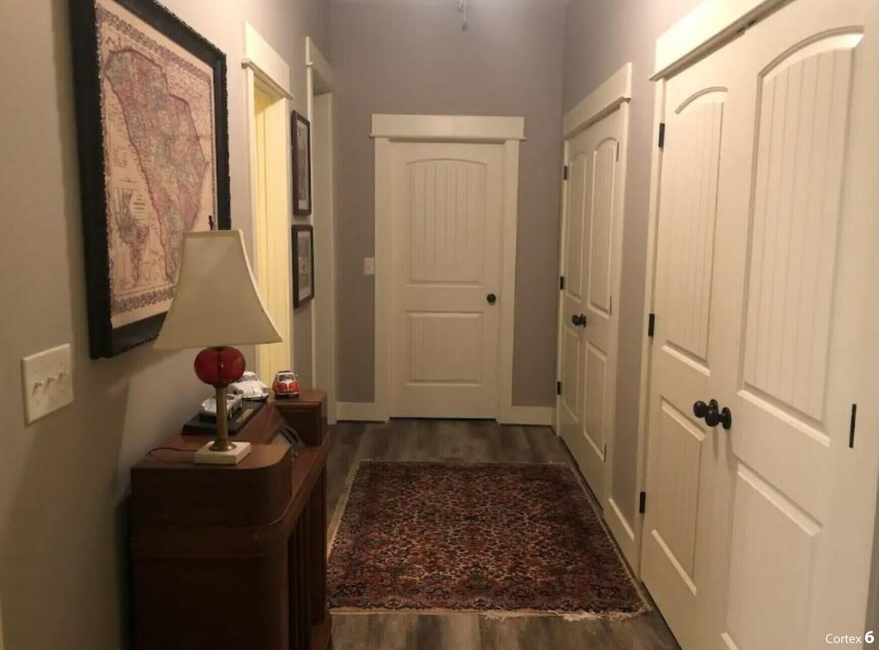 A hallway with a wooden floor, a rug, a lamp, and a map on the wall.