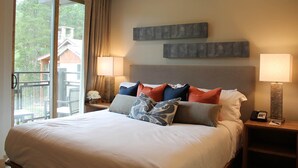 A hotel room with a large bed, two bedside lamps, a nightstand, and a view of a balcony with outdoor furniture. - The Premier Ski-in Ski-out Address in all of Colorado - Unit LIcense 81047001. (Breckenridge)