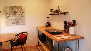 A compact kitchen with a wooden countertop, a blender, a cutting board, and a shelf with kitchen utensils and glassware. - Sunset Cottage with Beautiful Blue Ridge Mountain Views (Clyde)