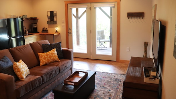 A living room with a brown sofa, a coffee table, a TV stand, and a sliding glass door leading to an outdoor patio. - Sunset Cottage with Beautiful Blue Ridge Mountain Views (Clyde)