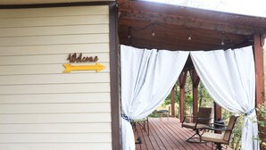 A wooden deck with a covered seating area, a sign reading "Welcome," and a directional arrow. - Sunset Cottage with Beautiful Blue Ridge Mountain Views (Clyde)
