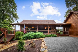 A wooden cabin with a porch, a flag, and a well-maintained garden. - Blackberry Lodge- Pet Friendly | Outdoor Firepit | Hot Tub (Blue Ridge)