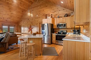 A wooden cabin interior with a kitchen featuring stainless steel appliances, wooden cabinets, and a bar area. - Blackberry Lodge- Pet Friendly | Outdoor Firepit | Hot Tub (Blue Ridge)