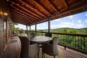 A covered outdoor area with a round table and wicker chairs, overlooking a forested landscape. - Blackberry Lodge- Pet Friendly | Outdoor Firepit | Hot Tub (Blue Ridge)