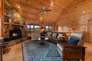 A cozy cabin interior with a stone fireplace, wooden walls, a ceiling fan, and a star decoration. - Blackberry Lodge- Pet Friendly | Outdoor Firepit | Hot Tub (Blue Ridge)
