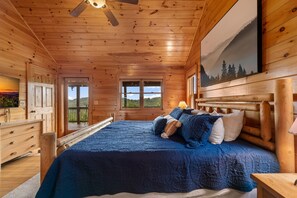A wooden cabin bedroom with a bed, pillows, a dresser, and a painting on the wall. - Blackberry Lodge- Pet Friendly | Outdoor Firepit | Hot Tub (Blue Ridge)