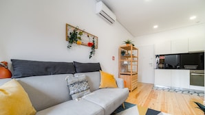 Un salón moderno con un sofá gris, cojines amarillos, una manta estampada y una estantería de madera.