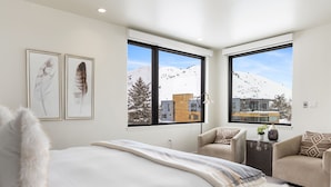 Ein modernes Schlafzimmer mit einem großen Bett, zwei Fenstern mit Blick auf die Berge, einer Couch und einem kleinen Tisch mit einer Vase.