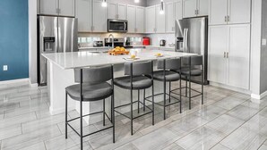Una cocina moderna con electrodomésticos de acero inoxidable, una isla central con taburetes de bar y armarios blancos.