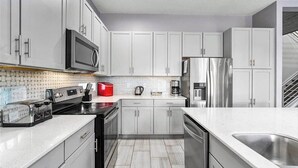 Una cocina moderna con armarios blancos, electrodomésticos de acero inoxidable y salpicadero de azulejos.