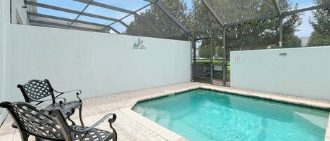 A covered outdoor swimming pool with a patio area and metal chairs.