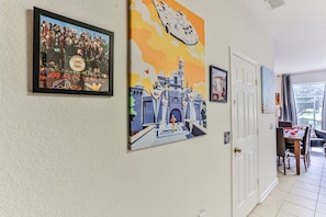 A hallway with framed artwork, a dining area, and a white door.