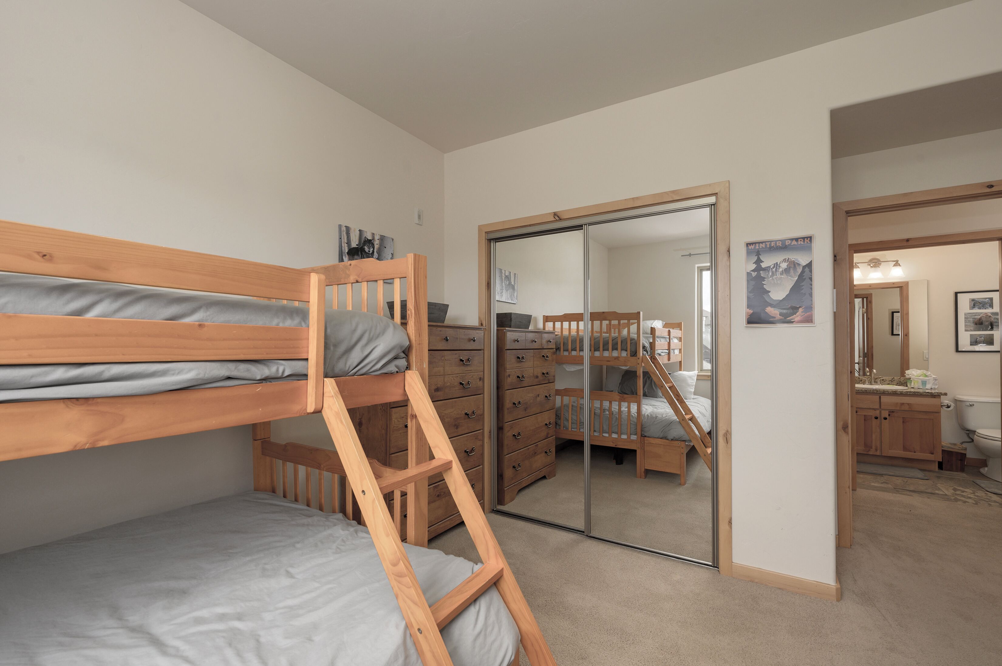 Een slaapkamer met stapelbedden, een houten dressoir, een spiegel en een poster aan de muur.