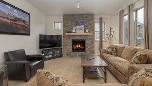Een woonkamer met een open haard, leren banken, een flatscreen televisie en een boekenplank.