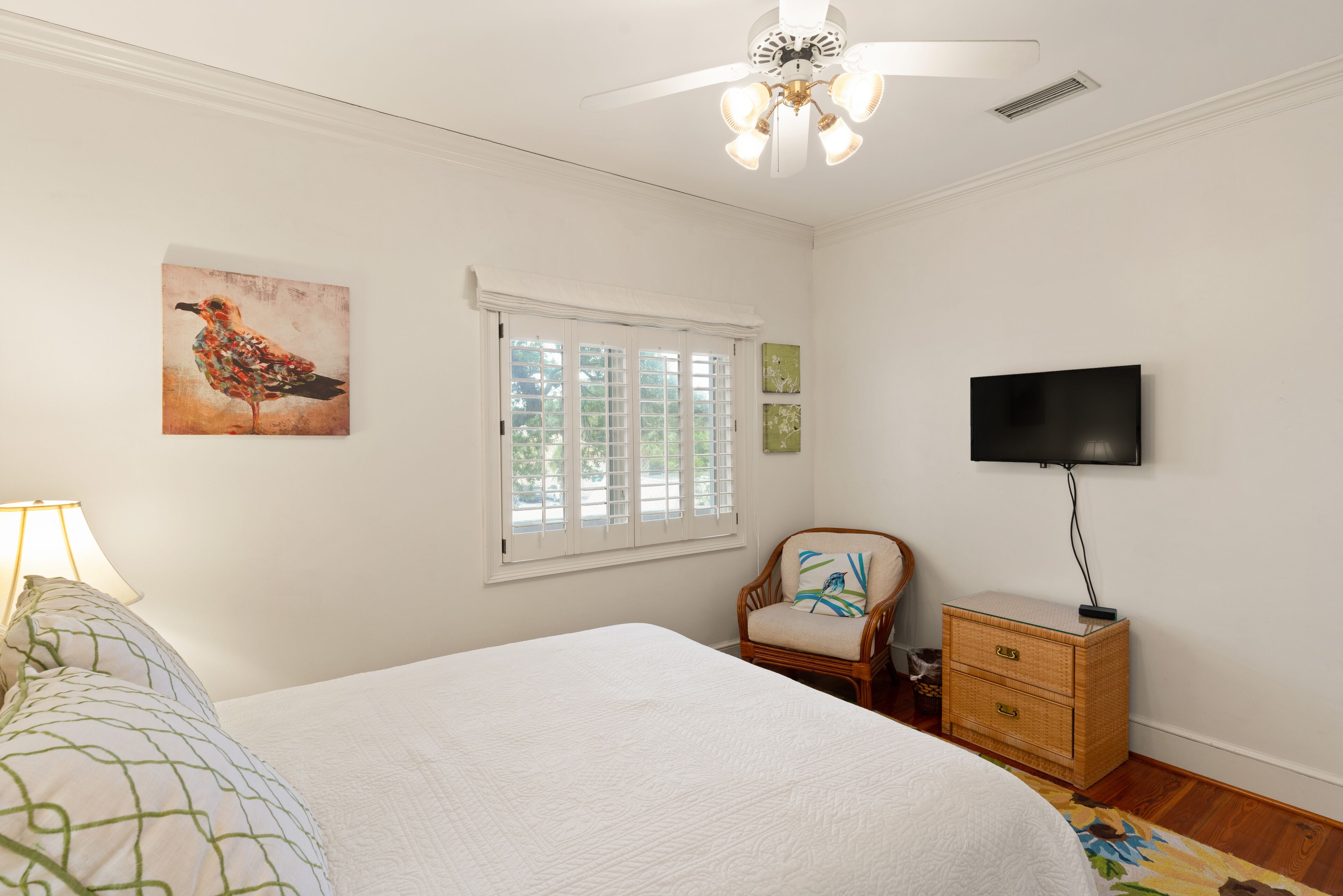 A bedroom with a bed, a chair, a TV, a window, and a ceiling fan.