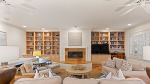 Un salon avec une cheminée, des canapés, une table basse et des étagères ornées d’objets décoratifs.