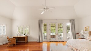 Une chambre spacieuse dotée d’un plancher en bois, d’un grand lit, d’un bureau avec une chaise et d’un ventilateur de plafond.