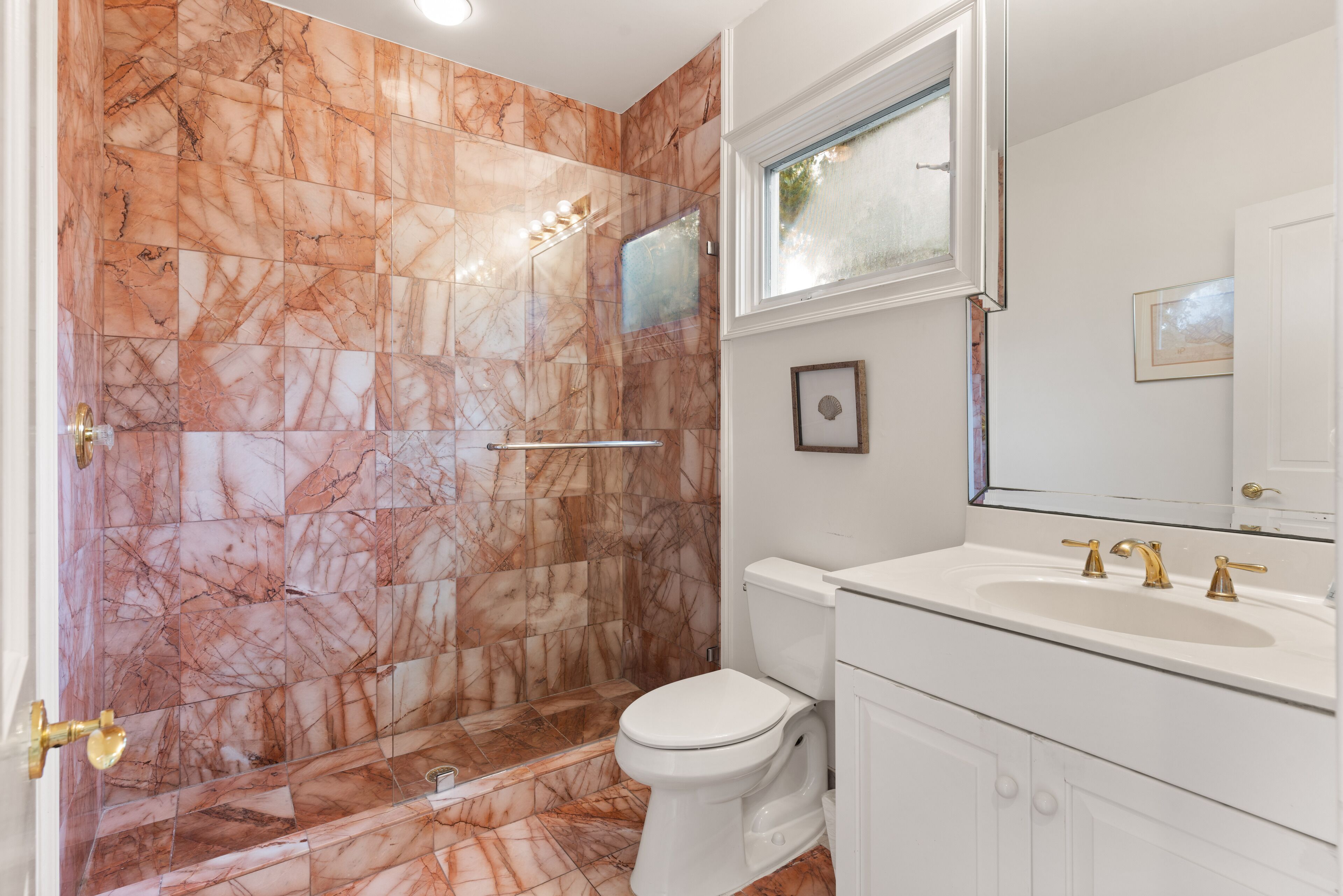 Ein Badezimmer mit Marmorwänden, einer weißen Toilette, einem Waschbecken mit Goldarmaturen und einem großen Spiegel.