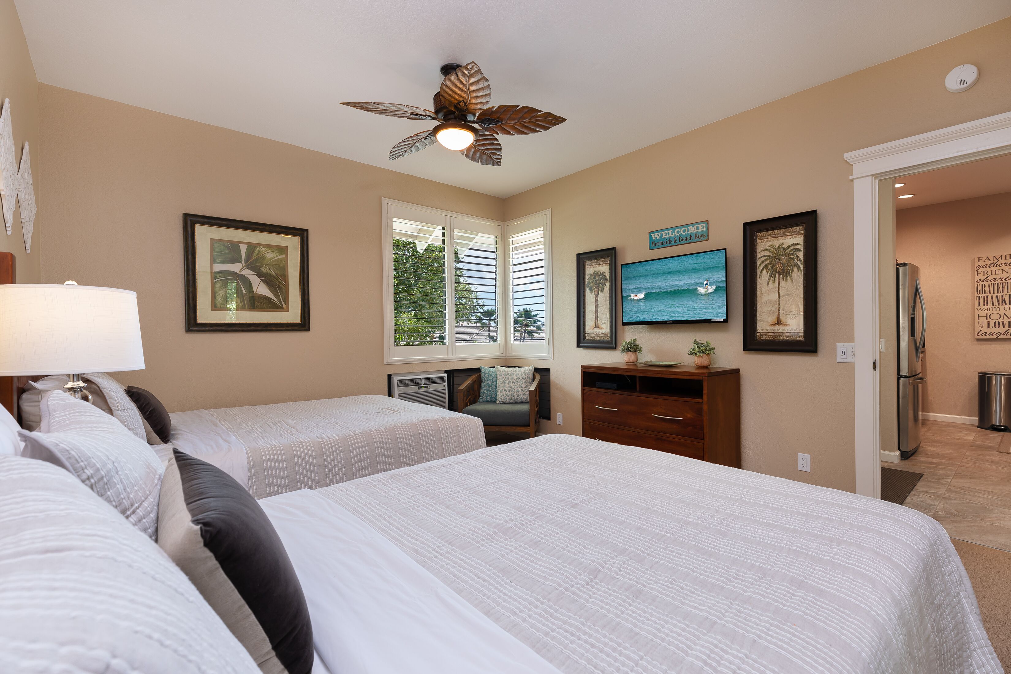 A hotel room with two beds, a ceiling fan, a TV, and a view of the ocean through the window.