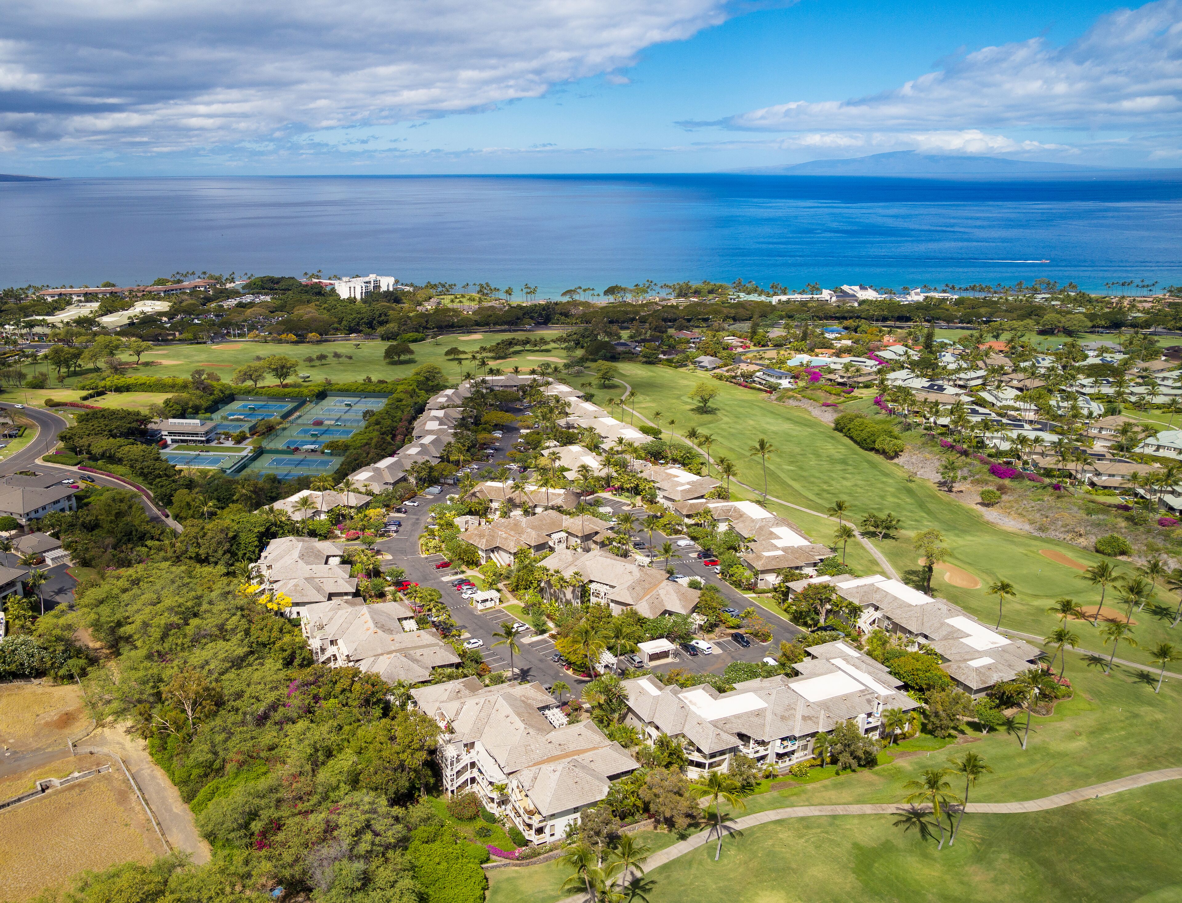 An aerial view of a residential area with houses, a golf course, and a large body of water in the background.
