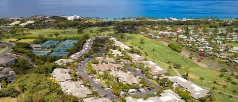 An aerial view of a residential area with houses, a golf course, and a large body of water in the background.