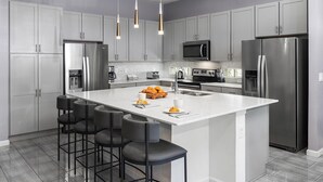 A modern kitchen with grey cabinets, stainless steel appliances, a central island with bar stools, and pendant lighting.