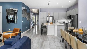 A modern kitchen with grey cabinets, a central island, and a dining area with a black table and chairs.