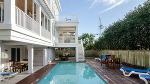 Una casa de dos pisos con piscina, mobiliario exterior y una terraza de madera.