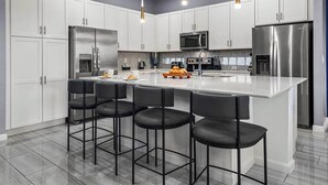 Una cocina moderna con armarios blancos, electrodomésticos de acero inoxidable y una isla central con taburetes de bar.