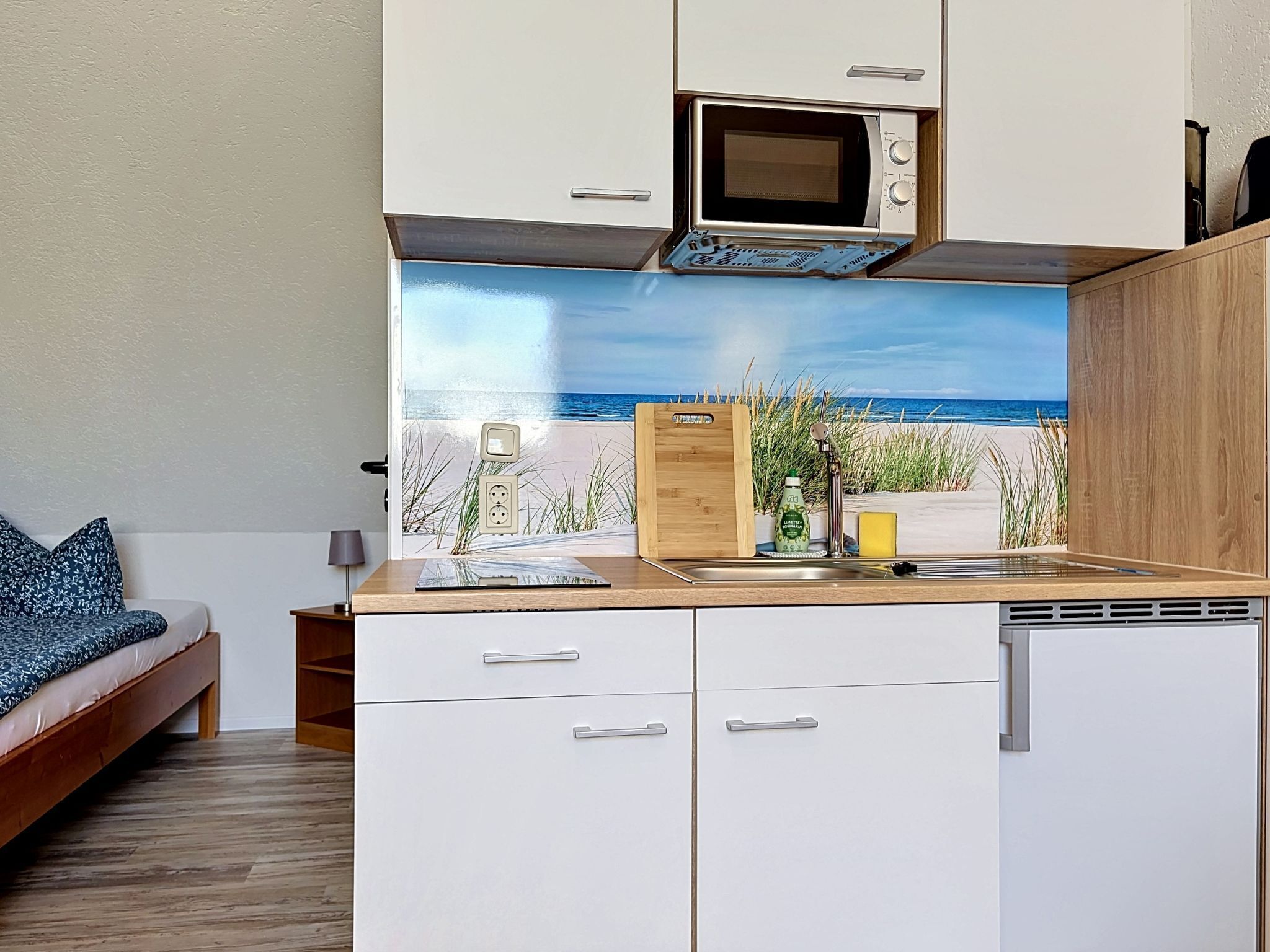 A compact kitchenette with a microwave, a sink, and a wooden cutting board.