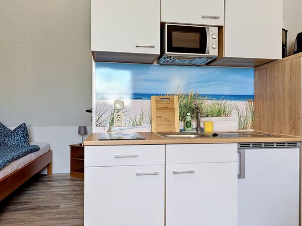 Een kleine keuken met een magnetron, een spoelbak en een houten snijplank.