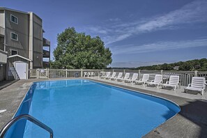 A rectangular pool with a metal safety railing, surrounded by white lounge chairs and a metal fence.