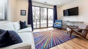 A modern living room with a sofa, armchairs, a colorful rug, a TV, and a large window with curtains. - Modern Downtown Masterpiece (Traverse City)