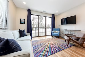 A modern living room with a sofa, armchairs, a colorful rug, a TV, and a large window with curtains. - Modern Downtown Masterpiece (Traverse City)