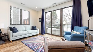 A modern living room with a sofa, a chair, a coffee table, and a large window with curtains. - Modern Downtown Masterpiece (Traverse City)