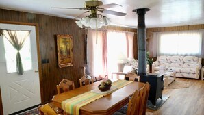 Uma sala de jantar com uma mesa de madeira, cadeiras, um ventilador de teto e uma lareira.