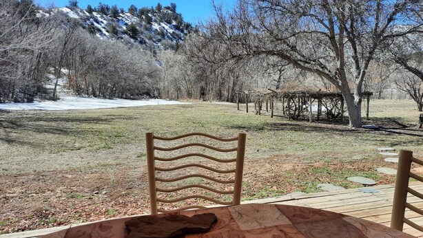 Mesa com toalha estampada, uma vela e uma cadeira rústica num jardim com vista para uma colina coberta de neve e árvores sem folhas.
