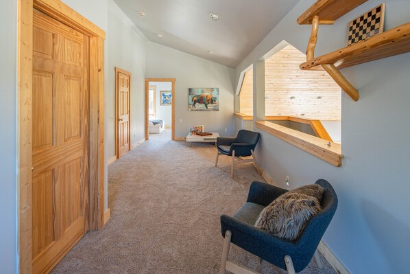 A hallway with wooden doors, a blue armchair, a wooden shelf with a chessboard, and a painting on the wall.
