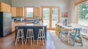 Una cucina moderna con mobili in legno, un'isola centrale con sgabelli, un'area pranzo con una panca e ampie finestre che offrono vista all'esterno.