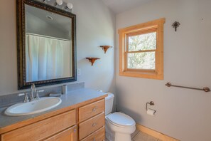 Ein Badezimmer mit einem Holzkosmetikschrank, einem weißen Waschbecken, einem großen Spiegel, einer Toilette und einem Fenster mit Holzrahmen.