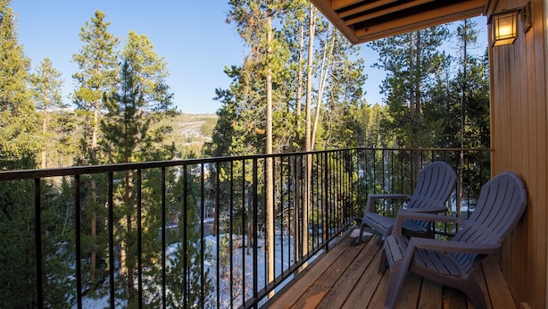 A wooden deck with Adirondack chairs overlooking a forested area with a view of a river. - Beaver Village Unit #1124 4 bedroom Beaver Village modern & extra unit amenities (Winter Park)