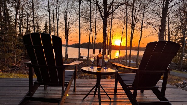Eine Holzterrasse mit zwei Adirondack-Stühlen, die auf einen See im Abendrot blicken.