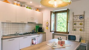 Une cuisine moderne avec des meubles blancs, un plan de travail en bois, un évier, une cuisinière et une fenêtre donnant sur un paysage verdoyant.