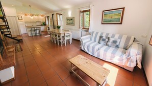 Un vaste espace de vie comprenant un canapé, un banc en bois, une table à manger avec des chaises, une cuisine à l’arrière-plan et un escalier menant à l’étage supérieur.